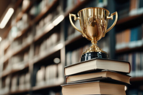 A golden trophy placed on a stack of books in a library, symbolizing academic excellence